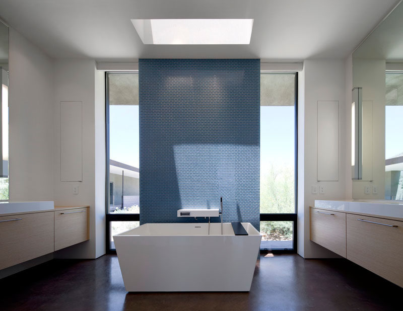 In this bathroom, tall windows and a skylight fill the space with natural light, while the blue tiled feature wall provides a focal point and privacy for when someone's taking a bath.