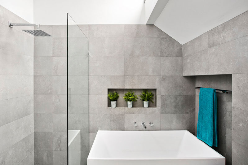 This master ensuite bathroom has been kept light and airy with the use of large light gray tiles, and a white bath. A small shelf and towel rack have been included in the design of the tiled walls.