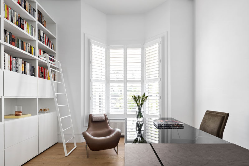 This bright white home office has shelving running along one wall with a bay window providing lots of natural light.