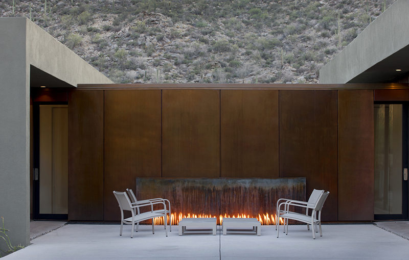 This outdoor fireplace is surrounded by weathering steel, and is located between two different areas of the home.