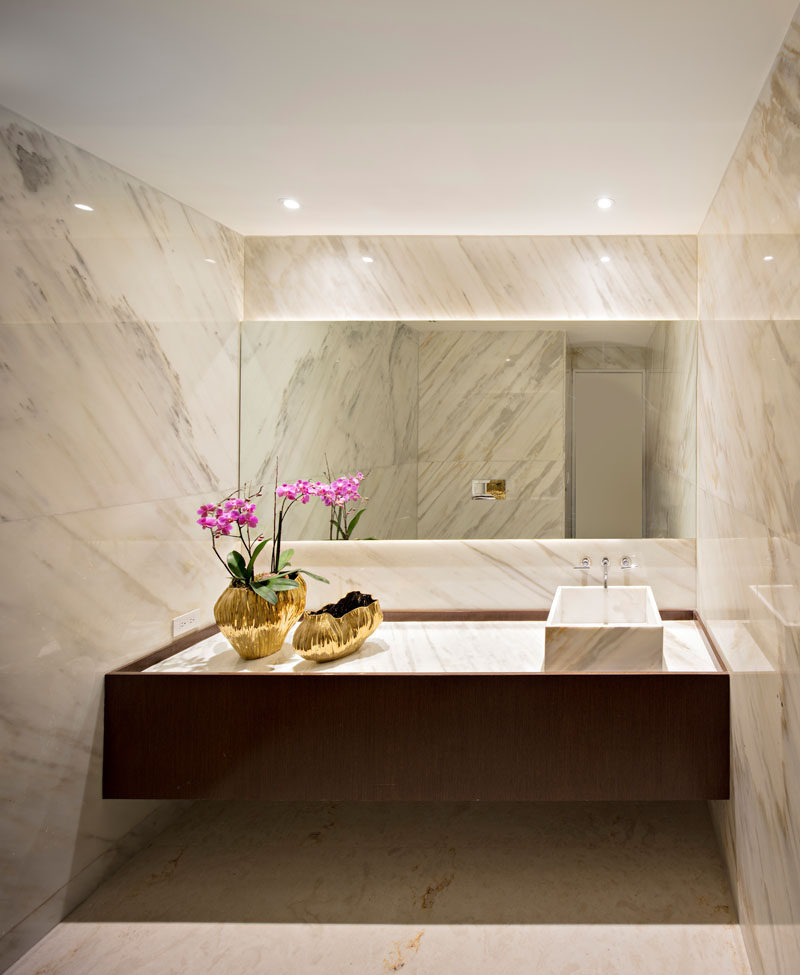 In this bathroom, stone covers the walls and a back-lit mirror creates soft ambient lighting.