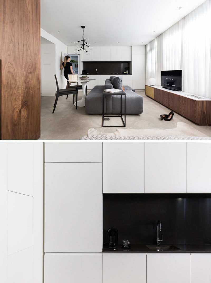 Along one wall of this small apartment is the kitchen with bright white cabinets and black backsplash. The integrated fridge gives the kitchen a seamless sleek look.