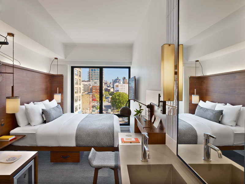 The hotel rooms at Arlo Hudson Square in NYC, have picturesque city views through a large window, and wood elements used throughout the design of the hotel make an appearance in the rooms too.