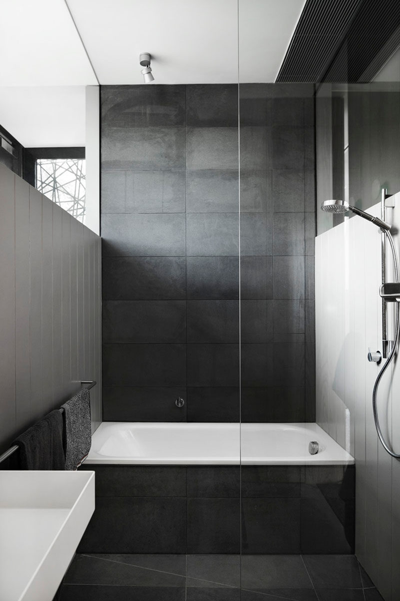 Bathroom Tile Ideas - Use Large Tiles On The Floor And Walls // Large dark tiles cover the floor, bath surround, and back wall of this bathroom, creating a dark dramatic look, but when paired with white walls it creates a sophisticated look.