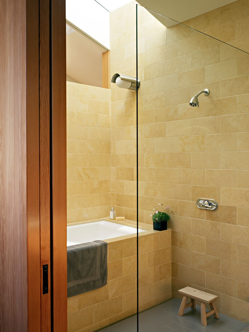 In this bathroom, light colored stone and a skylight keep the space bright and welcoming.