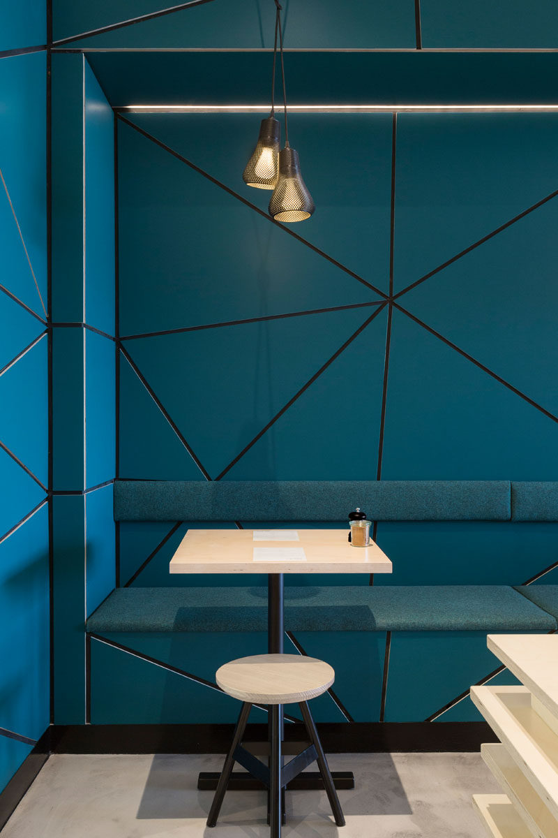 In this modern cafe, teal blue walls with a tessellated pattern have been paired with concrete flooring and light wood furniture.
