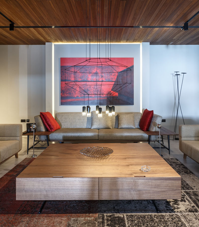This formal lounge room has a minimal line chandelier, with bold red artwork and cushions adding a touch of color.