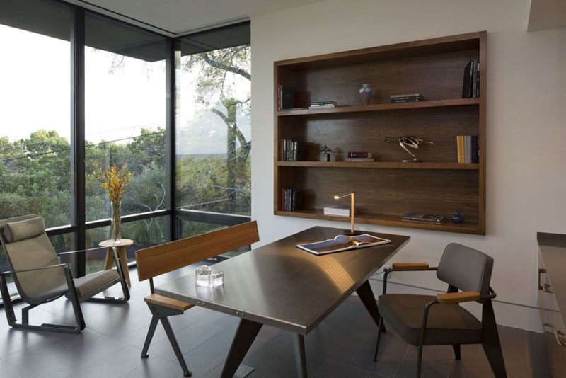 This home office has with large windows and built-in wooden shelving.