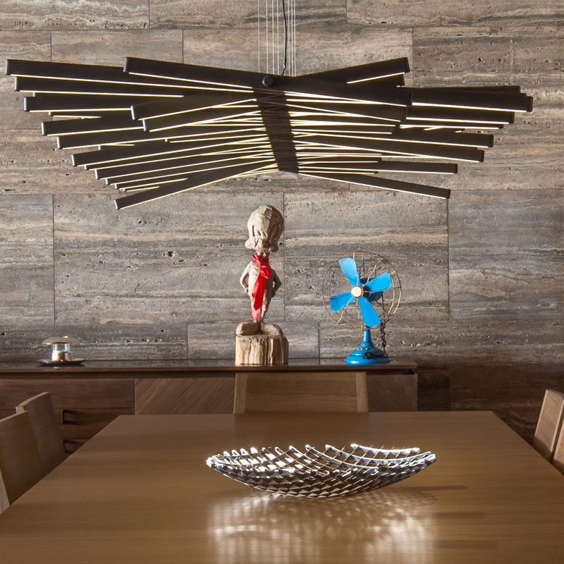 A sculptural light hangs directly above this dining table, while a wall of silver grey travertine runs the length of the home.