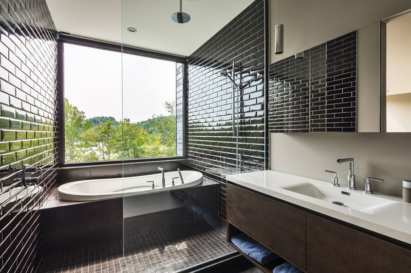This ensuite bathroom has the shower and built-in bathtub partitioned off with a glass screen, while the black tile draws your eye to the tree-top view outside.