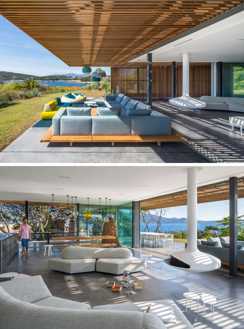 The outdoor living room f this modern villa seamlessly transitions into the indoor living room, that has a curved couch and a hanging fireplace.