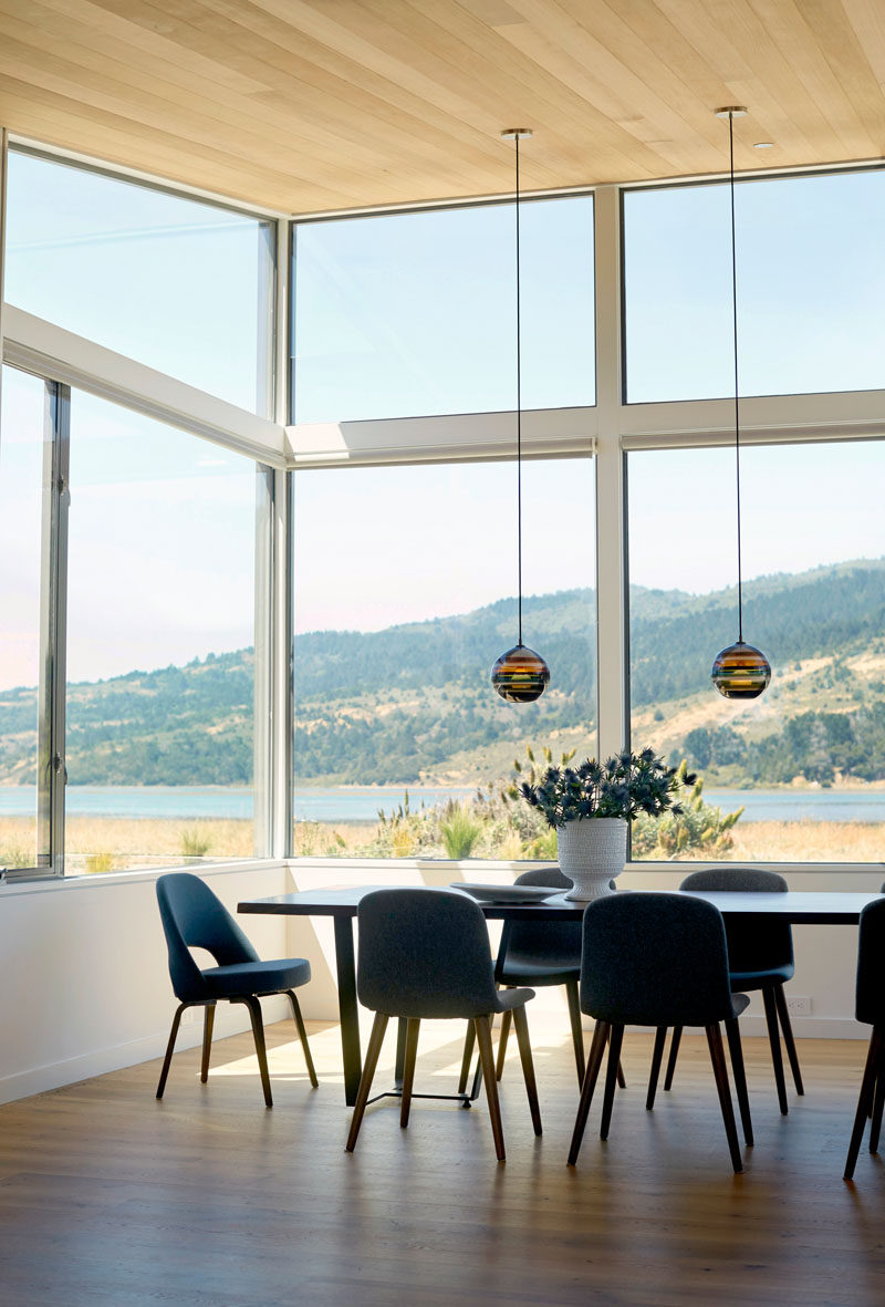 In this dining room, two delicate pendant lamps hang from the ceiling, while the large windows allow for plenty of natural light to fill the interior and they frame the surrounding views.