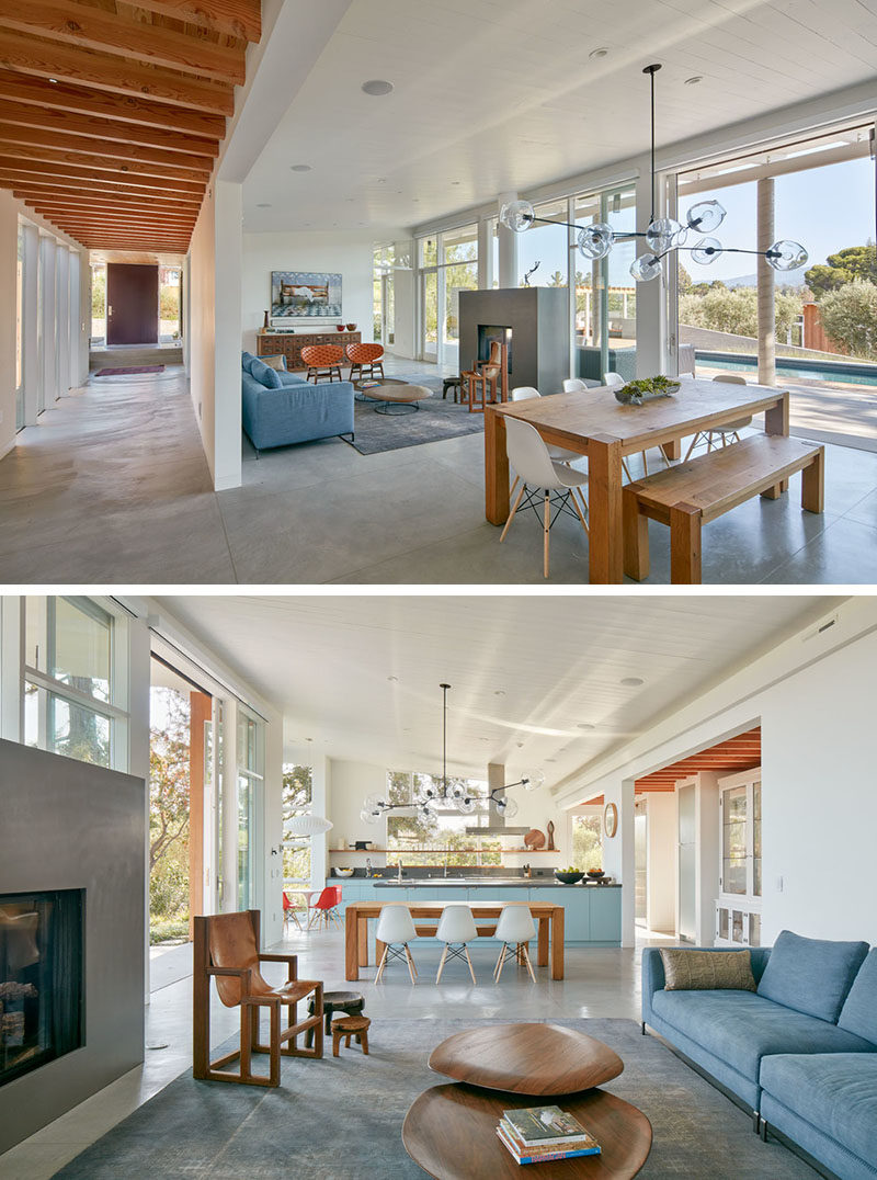 In this living area, there's a double-sided fireplace that can be enjoyed from the living room and the outdoor living space too. Between the living area and the kitchen is a large wooden dining table with a sculptural pendant light.