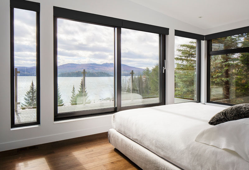 This master bedroom has black window frames that contrast the white walls, and a door leads to a private balcony with amazing lake and mountain views.