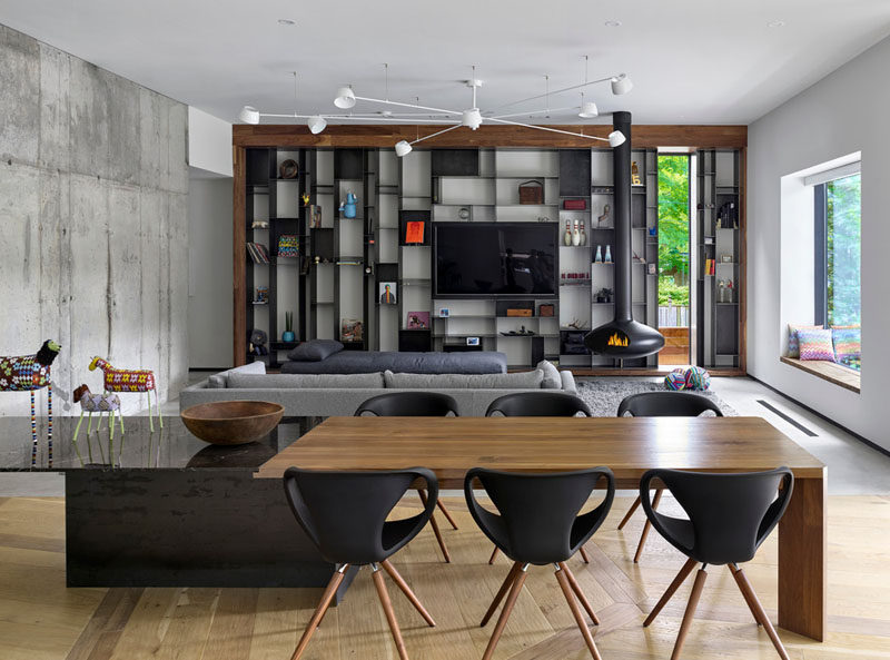 In this interior, a long dining table divides the open floor plan. On one end is the family room with a custom designed metal metal bookcase by Commute Design, and a suspended black wood-burning fireplace.