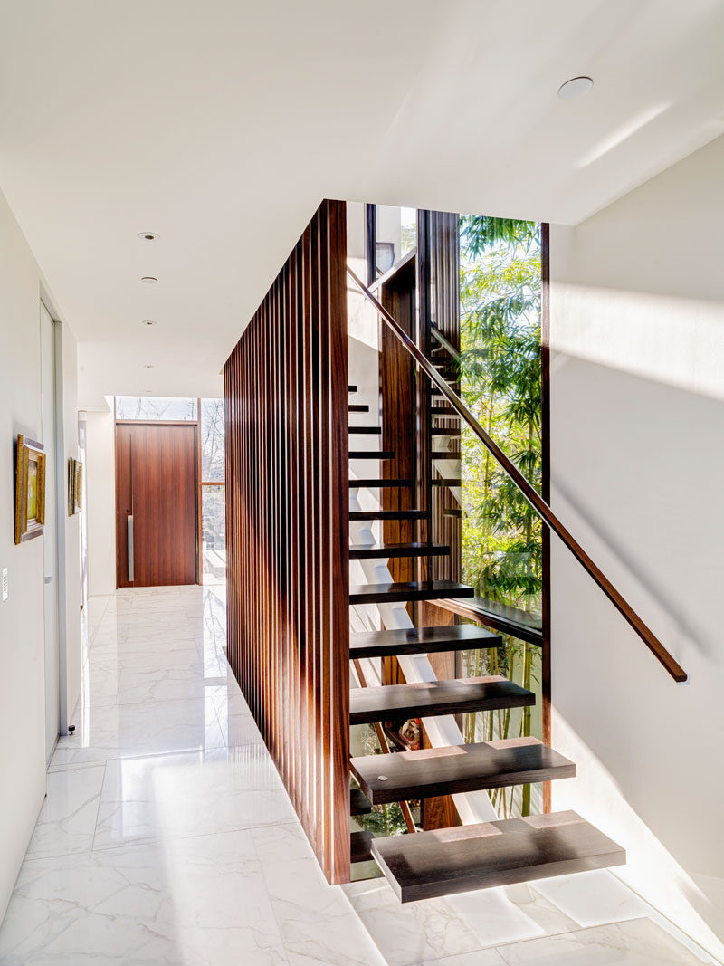 This modern wood staircase matches the wood used on the front door, and is a strong contrast against the white walls and white marble flooring.