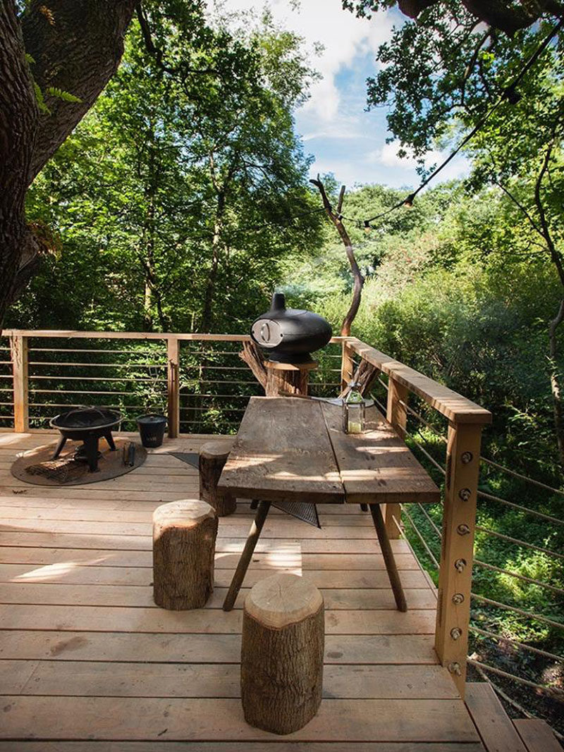This modern treehouse has a bbq and dining area on the deck that wraps around a tree.